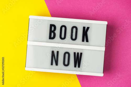 Book now - text on a display lightbox on yellow and pink background.