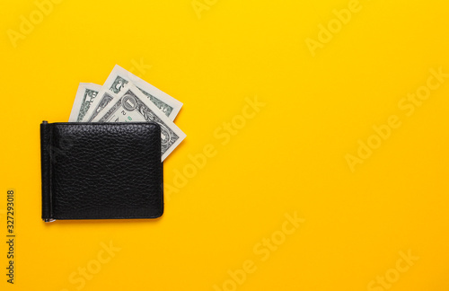 Black purse with dollar banknotes on yellow background. Flat lay, top view, copy space.