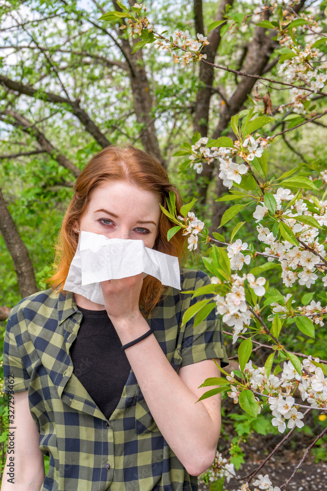 Season allergy to flowering plants pollen. Young woman with paper handkerchief in hand covering her nose in garden. Teen girl sneezing against blossoming trees. Seasonal allergy prevention Season allergy to flowering plants pollen. Young woman with paper handkerchief in hand covering her nose in garden. Teen girl sneezing against blossoming trees. Seasonal allergy prevention