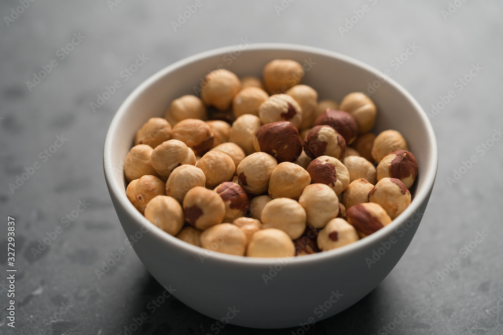 roasted hazelnuts in white bowl on concrete background