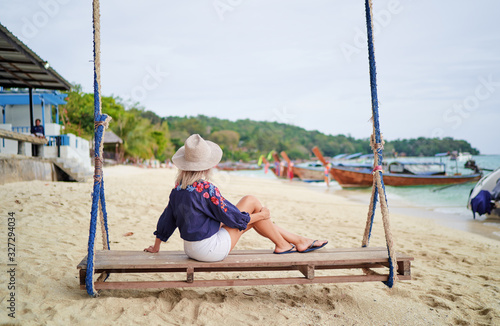 Relax vacation. Young woman in purple dress swinging on teeterboard near the sea with fisshing longtail boats in Thailand. photo