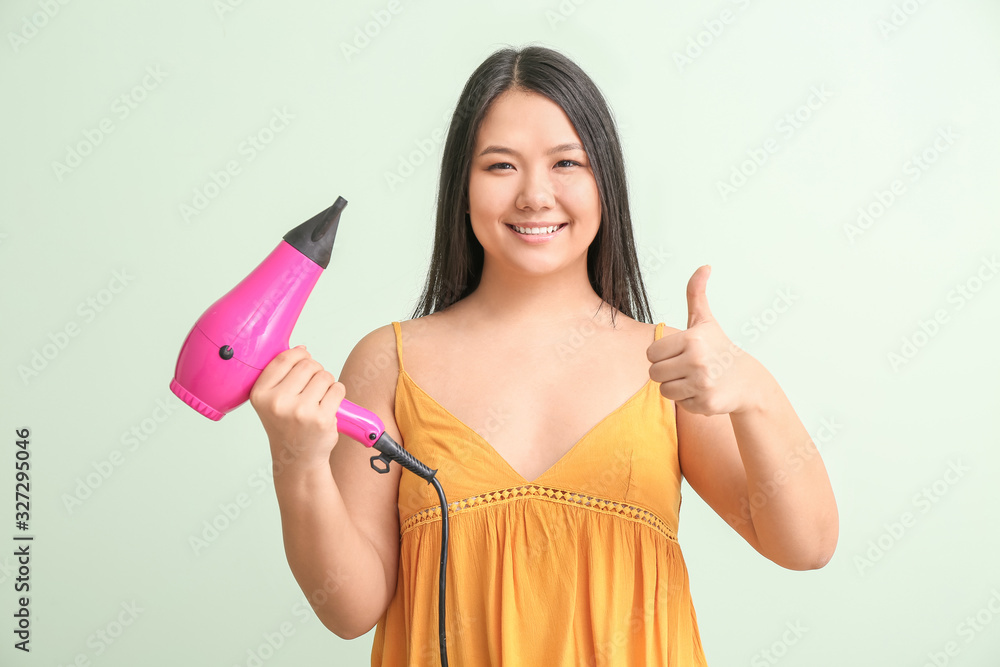 Beautiful Asian woman with hair dryer on color background Beautiful Asian woman with hair dryer on color background