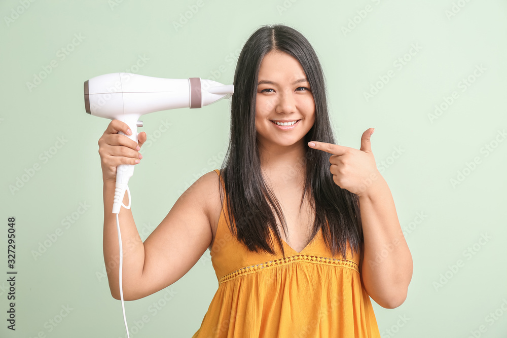 Beautiful Asian woman with hair dryer on color background Beautiful Asian woman with hair dryer on color background