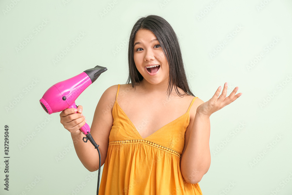 Surprised Asian woman with hair dryer on color background Surprised Asian woman with hair dryer on color background