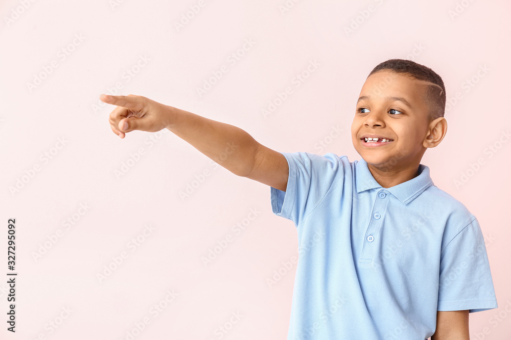 Happy smiling African-American boy pointing at something on color background Happy smiling African-American boy pointing at something on color background