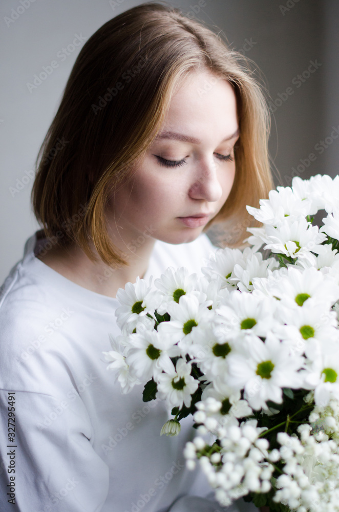 portrait of a young beautiful girl with blond hair and a short haircut with white flowers in her hands on a white background, the concept of beauty and health portrait of a young beautiful girl with blond hair and a short haircut with white flowers in her hands on a white background, the concept of beauty and health