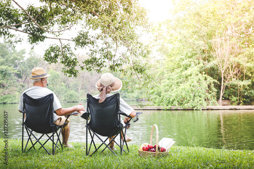 Elderly couple Sitting on a black chair in a shady garden And there is a picnic basket for bread and fruit. Senior community life concept Creating happiness and health care. copy space