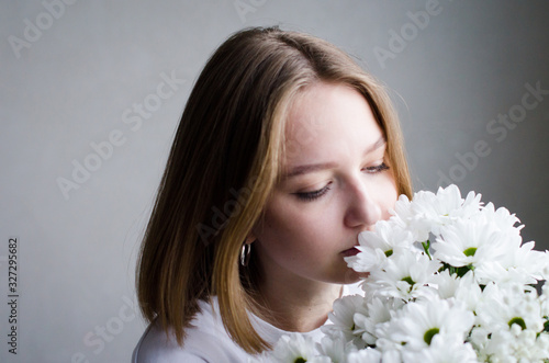 portrait of a young beautiful girl with blond hair and a short haircut with white flowers in her hands on a white background, the concept of beauty and health
