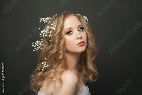 Portrait of sweet blonde girl with long healthy curly hairdo on dark background