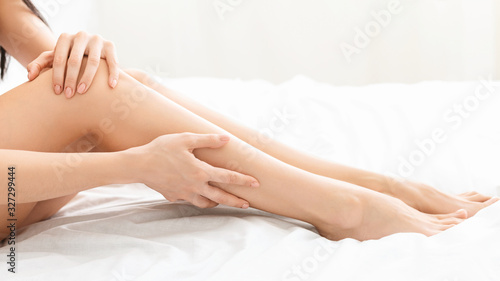 Young woman touching smooth skin of her legs in bed