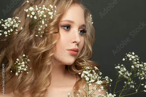 Lovely young woman with long blonde curly hairstyle and white flowers on dark background