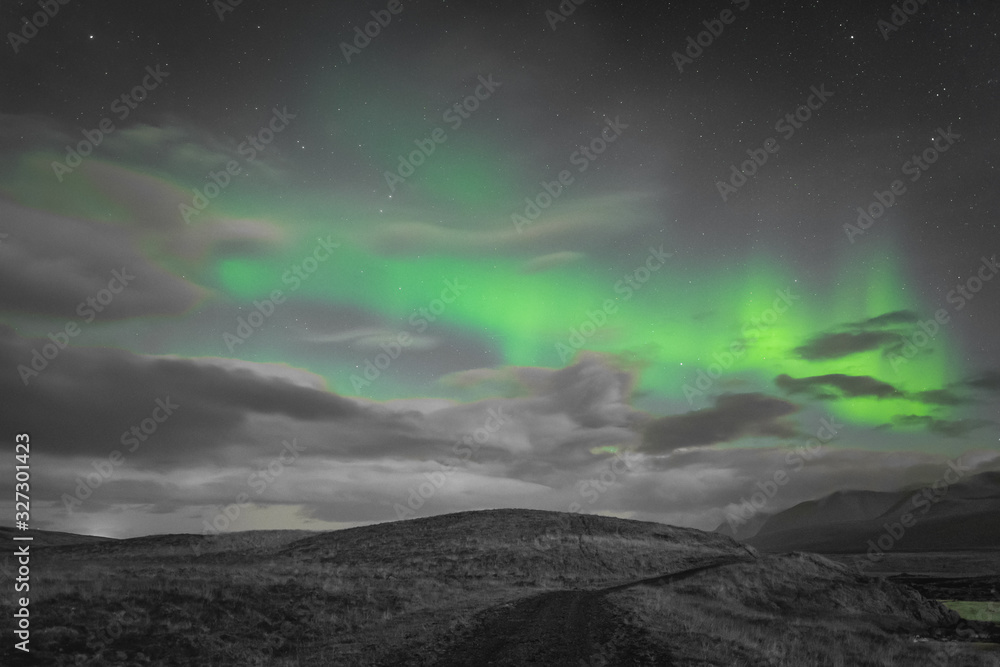 Aurora Borealis in Iceland northern lights bright beams rising green over hiking path and clouds in black white and accent color