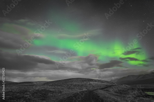 Aurora Borealis in Iceland northern lights bright beams rising green over hiking path and clouds in black white and accent color