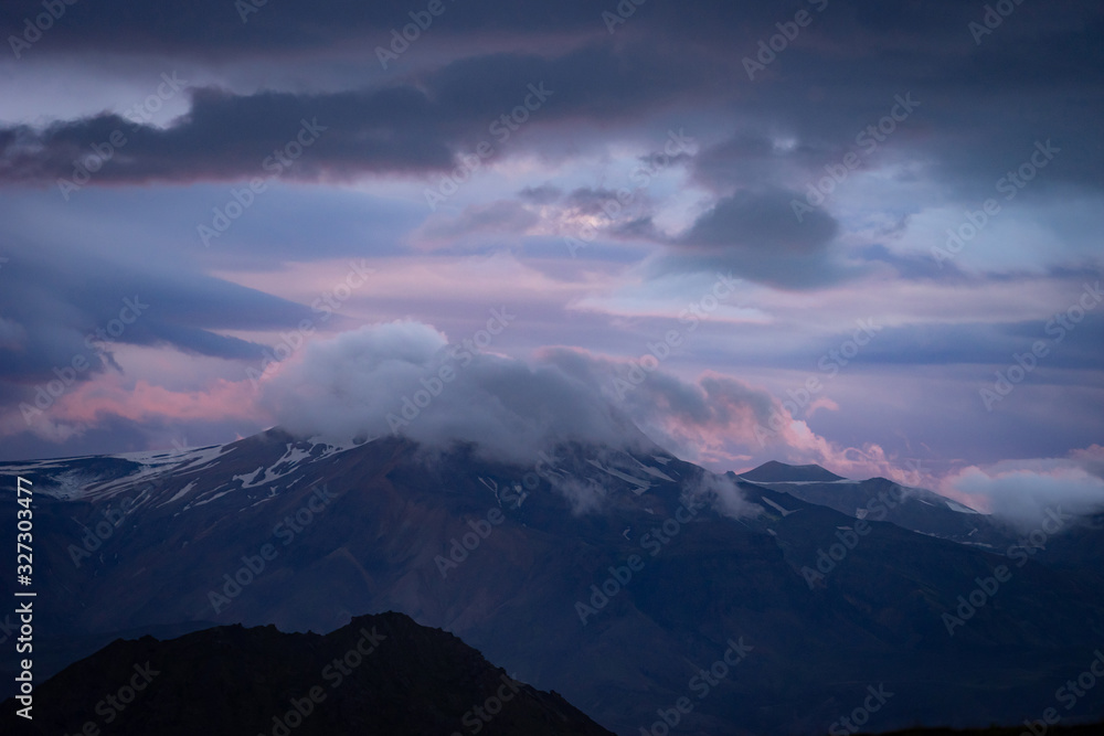 Mountain peak with snow and clouds during dramatic and colorful sunset