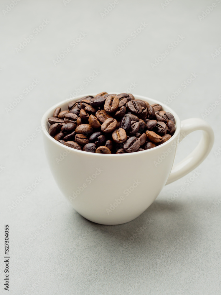 Close-up and side view of roasted Thai coffee beans in white coffee cup on light gray background with area for copy space. Close-up and side view of roasted Thai coffee beans in white coffee cup on light gray background with area for copy space.