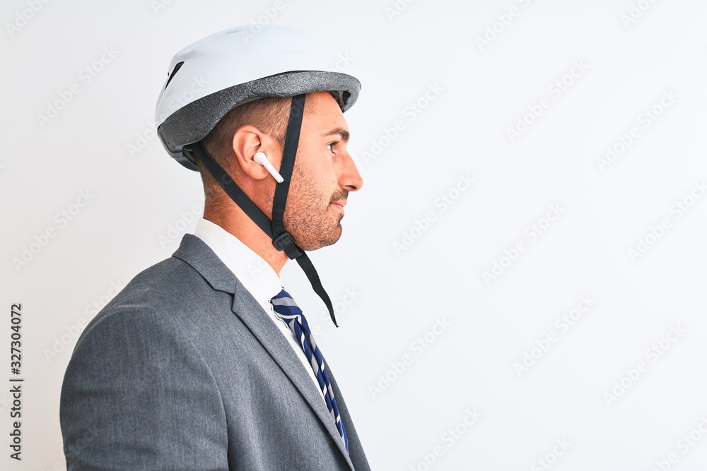 Fototapeta premium Young handsome business man bike helmet and wireless earphones over isolated background looking to side, relax profile pose with natural face with confident smile.