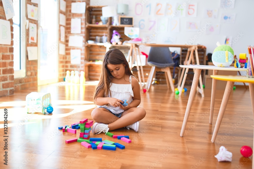 Adorable toddler sitting on the floor. Playing with wooden building blocks at kindergarten