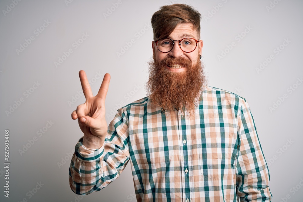 Handsome Irish redhead man with beard wearing glasses and hipster shirt smiling with happy face winking at the camera doing victory sign. Number two. Handsome Irish redhead man with beard wearing glasses and hipster shirt smiling with happy face winking at the camera doing victory sign. Number two.