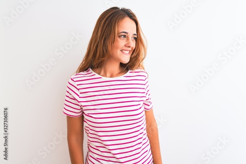 Young redhead woman wearing striped casual t-shirt stading over white isolated background looking away to side with smile on face, natural expression. Laughing confident. © Krakenimages.com