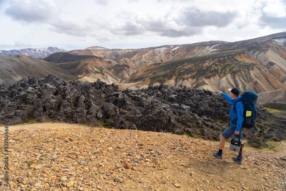 Hiker with backpack in the Landmannalaugar Valley. Iceland. Colorful mountains on the Laugavegur hiking trail. The combination of layers of multi-colored rocks, minerals, grass and moss