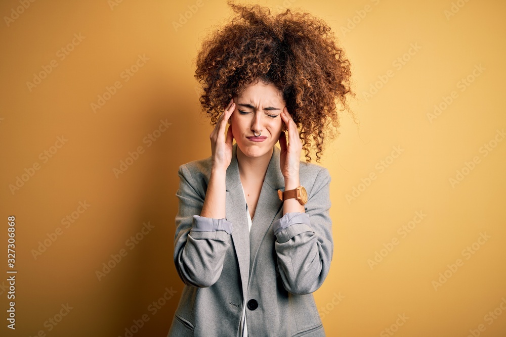 Young beautiful businesswoman with curly hair and piercing wearing elegant jacket suffering from headache desperate and stressed because pain and migraine. Hands on head. Young beautiful businesswoman with curly hair and piercing wearing elegant jacket suffering from headache desperate and stressed because pain and migraine. Hands on head.