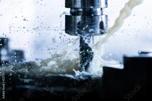 a process of vertical cnc steel milling with external water coolant streams, splashes and a lot of metal chips, high contrast photo