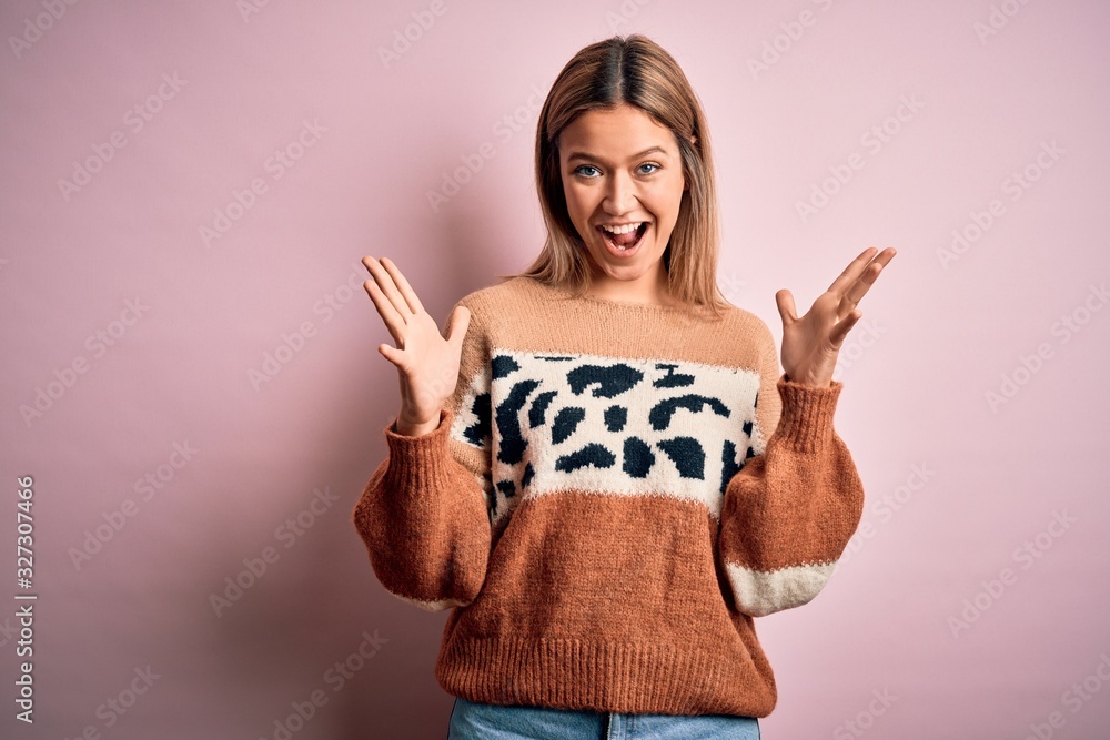 Young beautiful blonde woman wearing fashion animal print sweater over pink background celebrating crazy and amazed for success with arms raised and open eyes screaming excited. Winner concept Young beautiful blonde woman wearing fashion animal print sweater over pink background celebrating crazy and amazed for success with arms raised and open eyes screaming excited. Winner concept