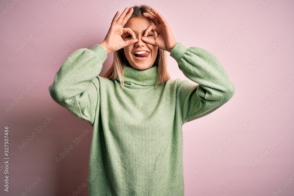 Young beautiful blonde woman wearing winter wool sweater over pink isolated background doing ok gesture like binoculars sticking tongue out, eyes looking through fingers. Crazy expression. Young beautiful blonde woman wearing winter wool sweater over pink isolated background doing ok gesture like binoculars sticking tongue out, eyes looking through fingers. Crazy expression.