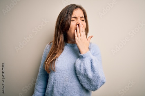 Beautiful young woman wearing casual winter sweater standing over isolated background bored yawning tired covering mouth with hand. Restless and sleepiness. © Krakenimages.com