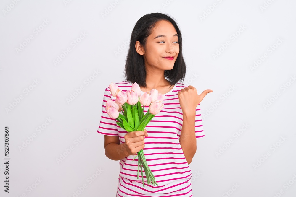 Young chinese woman holding bouquet of roses standing over isolated white background pointing and showing with thumb up to the side with happy face smiling Young chinese woman holding bouquet of roses standing over isolated white background pointing and showing with thumb up to the side with happy face smiling