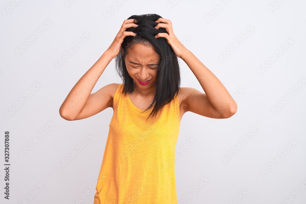 Young chinese woman wearing yellow casual t-shirt standing over isolated white background suffering from headache desperate and stressed because pain and migraine. Hands on head. Young chinese woman wearing yellow casual t-shirt standing over isolated white background suffering from headache desperate and stressed because pain and migraine. Hands on head.