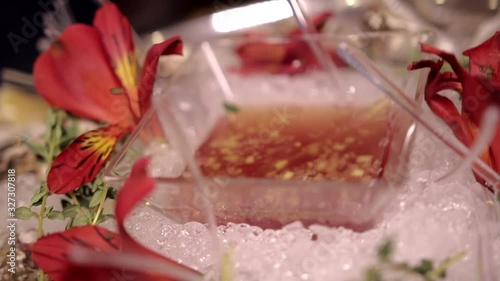 Set of fresh oysters in shells with lemon slices, herbs, red alstroemeria flowers and a transparent plate of traditional mignonette sauce in ice. Seafood on metal tray, close-up.