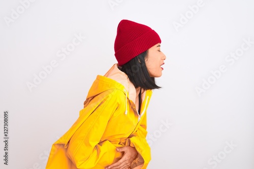 Young beautiful chinese woman wearing raincoat and wool cap over isolated white background with hand on stomach because indigestion, painful illness feeling unwell. Ache concept. © Krakenimages.com