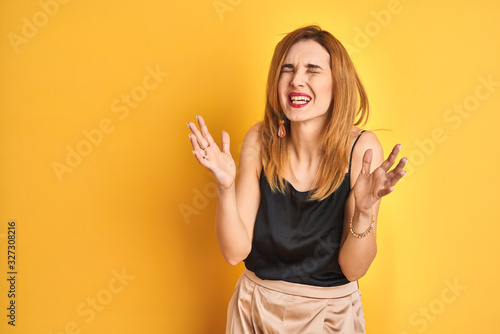 Redhead caucasian business woman standing over yellow isolated background celebrating mad and crazy for success with arms raised and closed eyes screaming excited. Winner concept