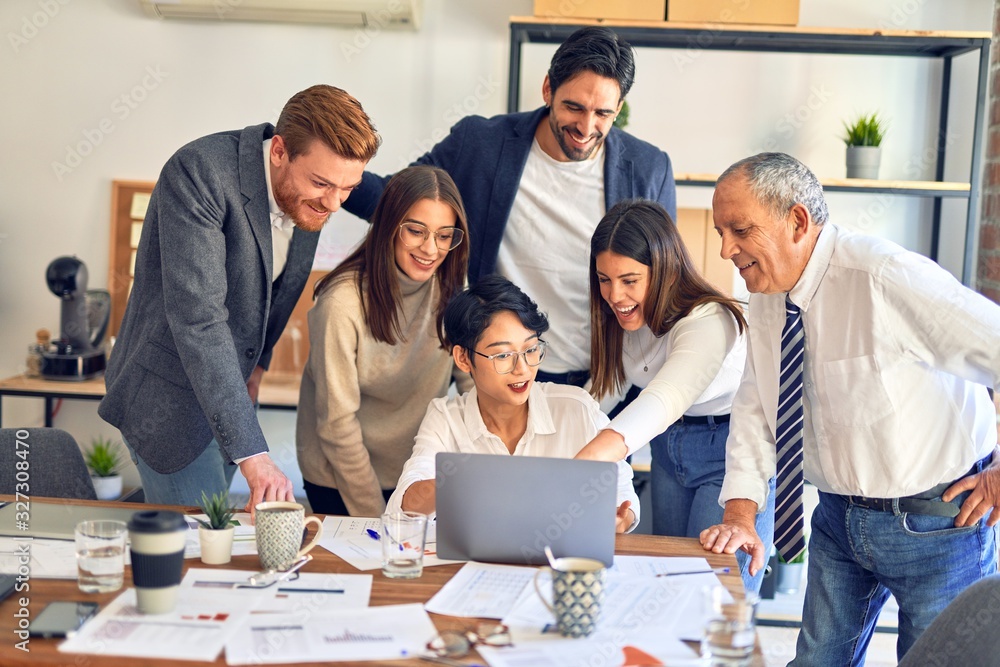 Group of business workers smiling happy and confident. One of them sitting and partners standing around. Working together with smile on face looking at the laptop at the office Group of business workers smiling happy and confident. One of them sitting and partners standing around. Working together with smile on face looking at the laptop at the office