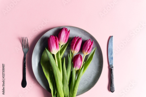 Plate with red tulips  fork and knife on pink background