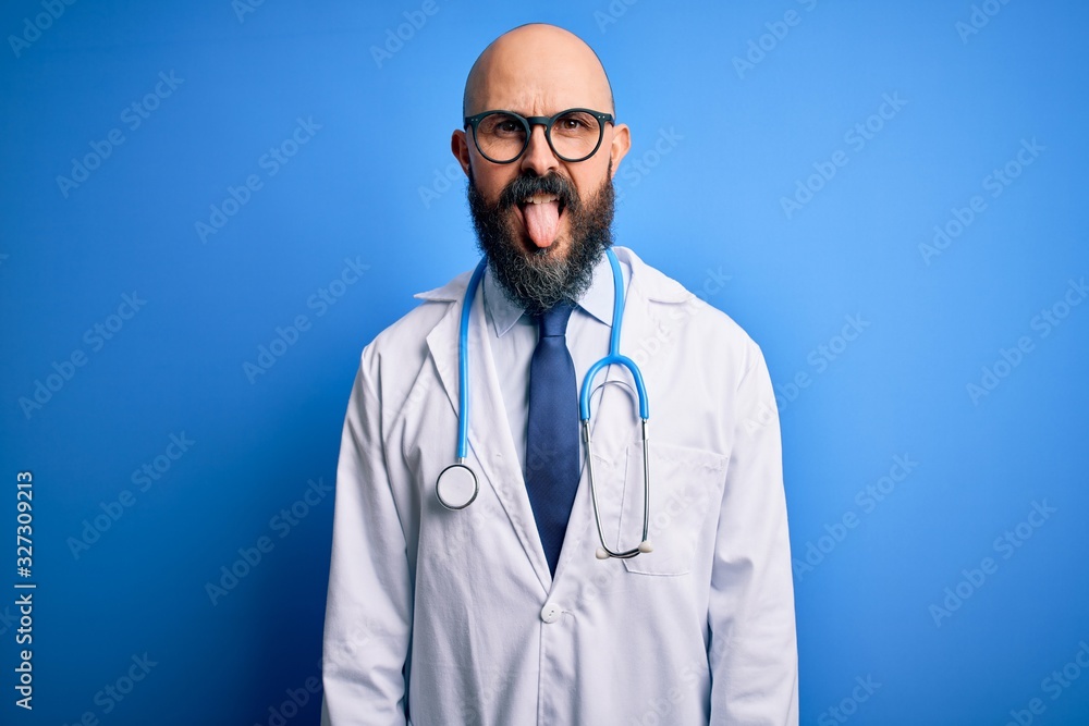 Handsome bald doctor man with beard wearing glasses and stethoscope over blue background sticking tongue out happy with funny expression. Emotion concept. Handsome bald doctor man with beard wearing glasses and stethoscope over blue background sticking tongue out happy with funny expression. Emotion concept.