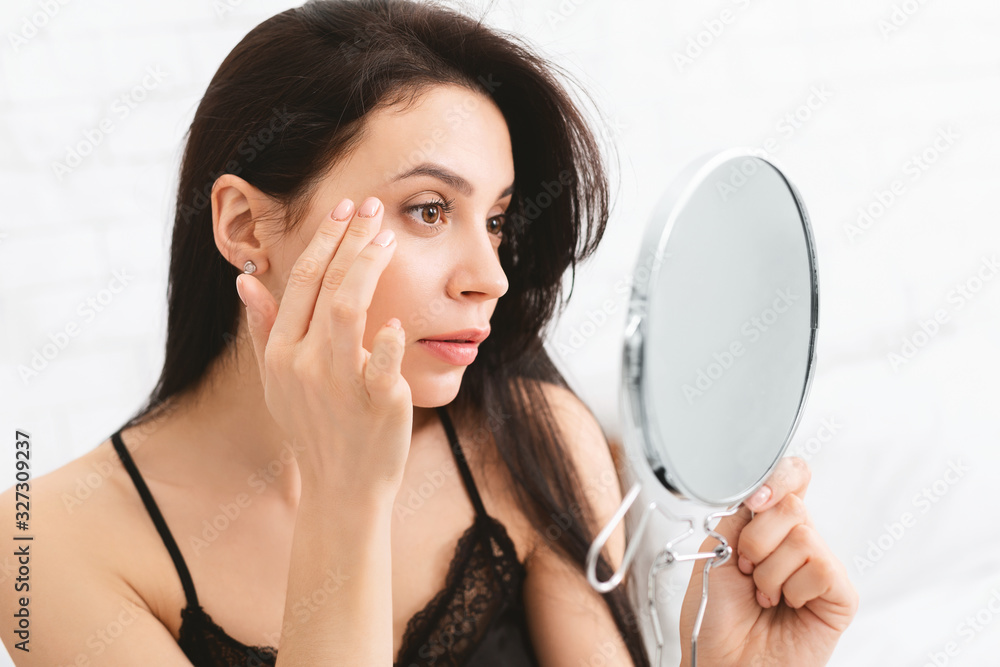 Young woman checking her wrinkles with mirror Young woman checking her wrinkles with mirror
