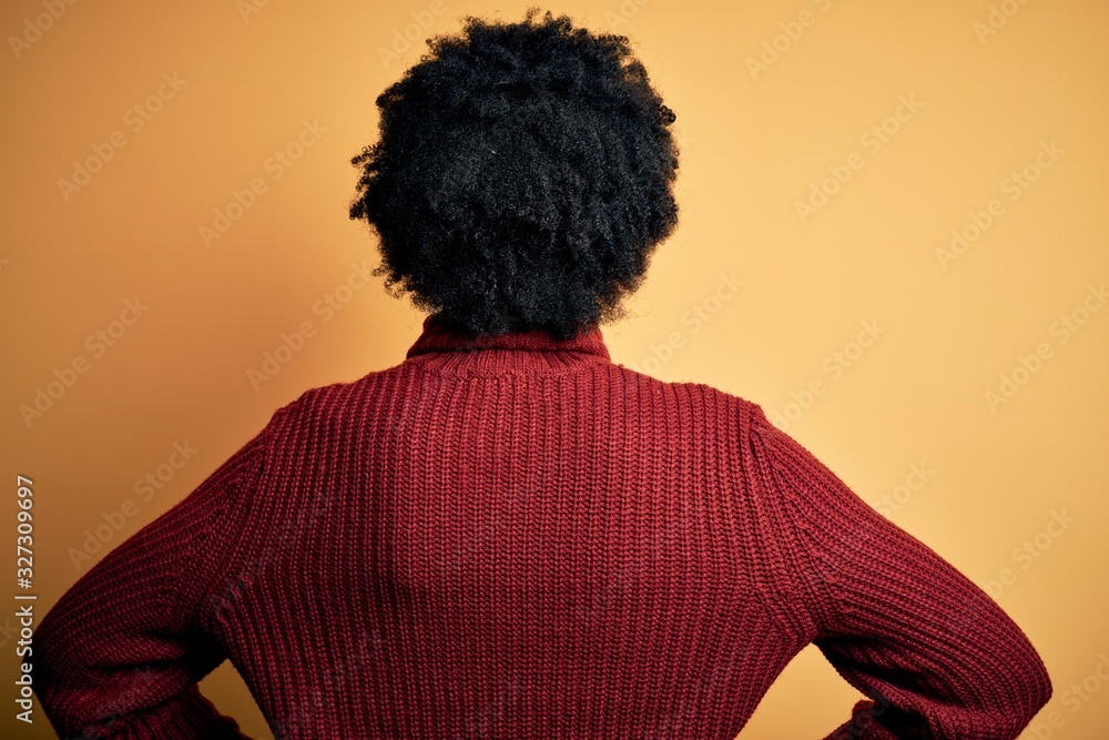 Young beautiful African American afro woman with curly hair wearing casual turtleneck sweater standing backwards looking away with arms on body Young beautiful African American afro woman with curly hair wearing casual turtleneck sweater standing backwards looking away with arms on body