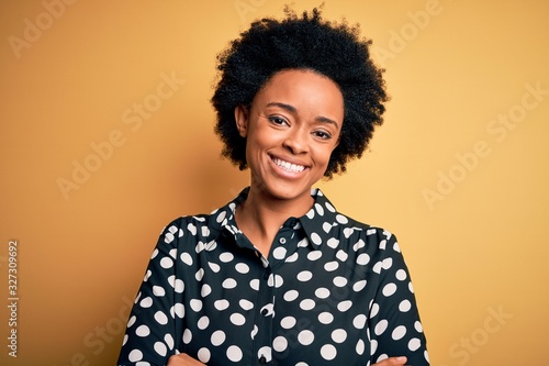 Young beautiful African American afro woman with curly hair wearing casual shirt standing happy face smiling with crossed arms looking at the camera. Positive person.