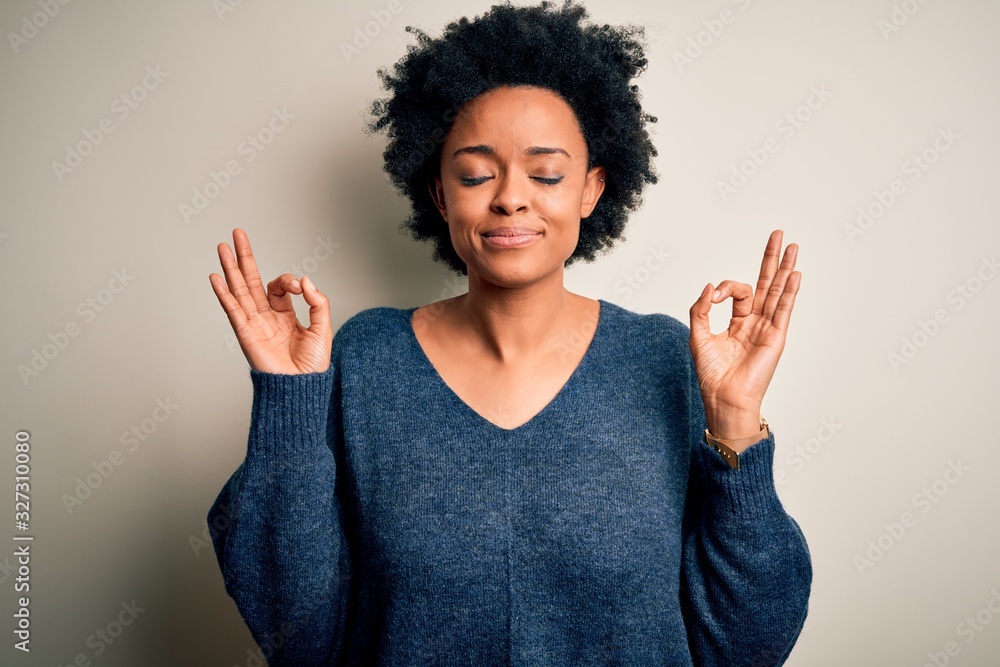 Young beautiful African American afro woman with curly hair wearing casual sweater relaxed and smiling with eyes closed doing meditation gesture with fingers. Yoga concept. Young beautiful African American afro woman with curly hair wearing casual sweater relaxed and smiling with eyes closed doing meditation gesture with fingers. Yoga concept.