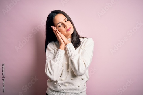 Young brunette woman with blue eyes wearing casual sweater over isolated pink background sleeping tired dreaming and posing with hands together while smiling with closed eyes. © Krakenimages.com