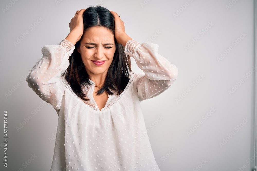 Young brunette woman with blue eyes wearing casual t-shirt over isolated white background suffering from headache desperate and stressed because pain and migraine. Hands on head. Young brunette woman with blue eyes wearing casual t-shirt over isolated white background suffering from headache desperate and stressed because pain and migraine. Hands on head.