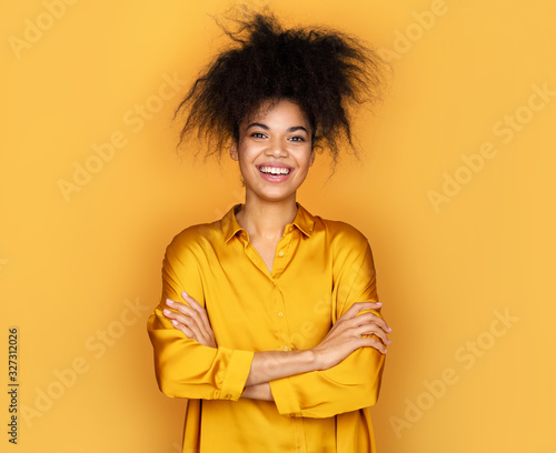 Smiling girl holds hands crossed. Photo of african american girl on yellow background