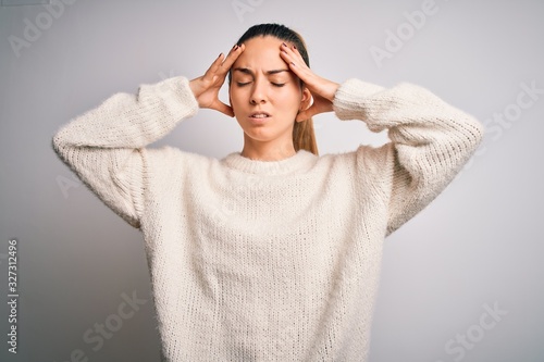 Young beautiful blonde woman with blue eyes wearing casual sweater over white background suffering from headache desperate and stressed because pain and migraine. Hands on head.