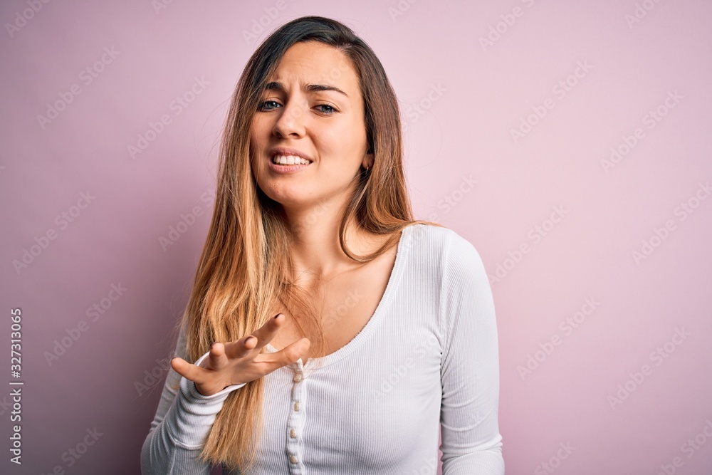 Young beautiful blonde woman with blue eyes wearing white t-shirt over pink background disgusted expression, displeased and fearful doing disgust face because aversion reaction. Young beautiful blonde woman with blue eyes wearing white t-shirt over pink background disgusted expression, displeased and fearful doing disgust face because aversion reaction.