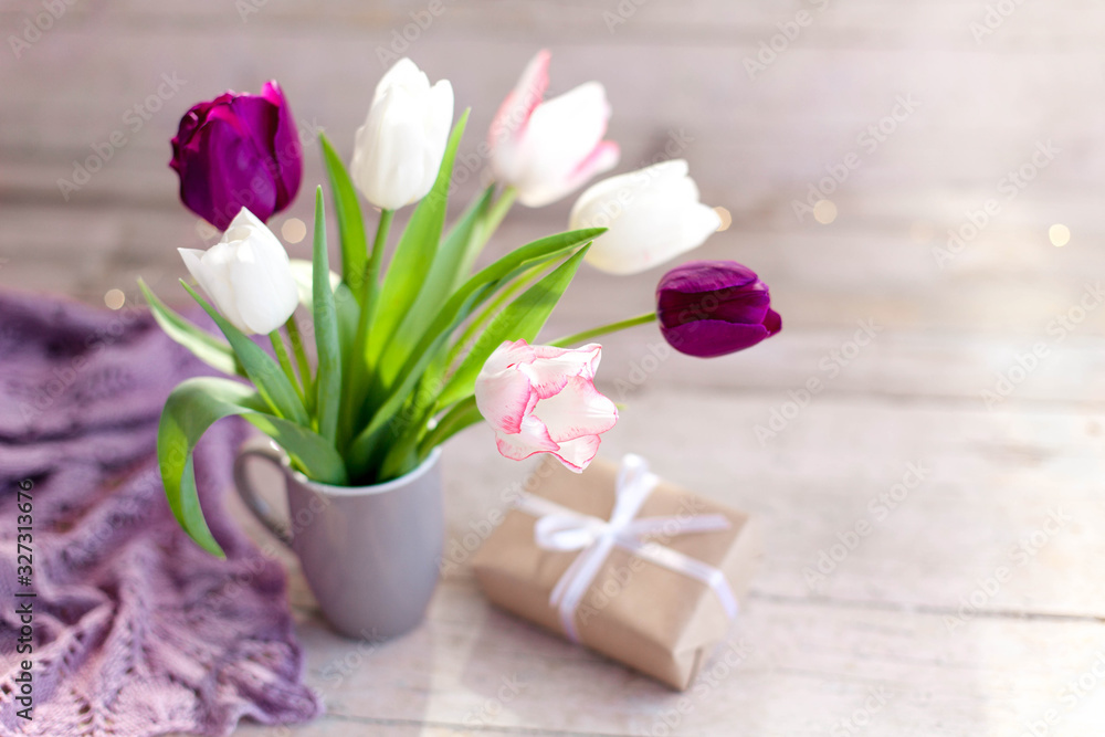 Spring flowers and gift box at wooden background. Blooming tulips in gray cup. Pink, white, lilac and purple bouquet in vase. Cozy still life. Copy space. Spring flowers and gift box at wooden background. Blooming tulips in gray cup. Pink, white, lilac and purple bouquet in vase. Cozy still life. Copy space.
