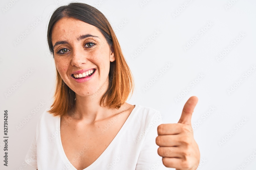Beautiful redhead woman wearing casual white t-shirt over isolated background happy with big smile doing ok sign, thumb up with fingers, excellent sign Beautiful redhead woman wearing casual white t-shirt over isolated background happy with big smile doing ok sign, thumb up with fingers, excellent sign