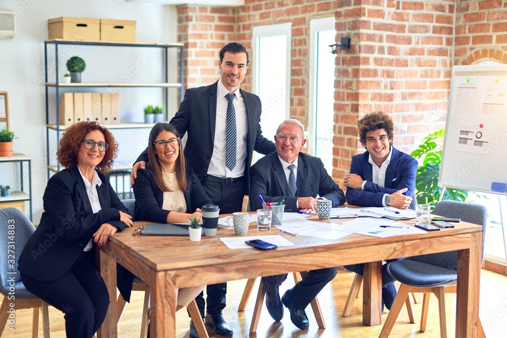 Group of business workers smiling happy and confident in a meeting. The boss standing and employees sitting with smile on face looking at the camera at the office Group of business workers smiling happy and confident in a meeting. The boss standing and employees sitting with smile on face looking at the camera at the office