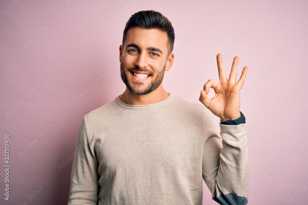 Young handsome man wearing casual sweater standing over isolated pink background smiling positive doing ok sign with hand and fingers. Successful expression. Young handsome man wearing casual sweater standing over isolated pink background smiling positive doing ok sign with hand and fingers. Successful expression.